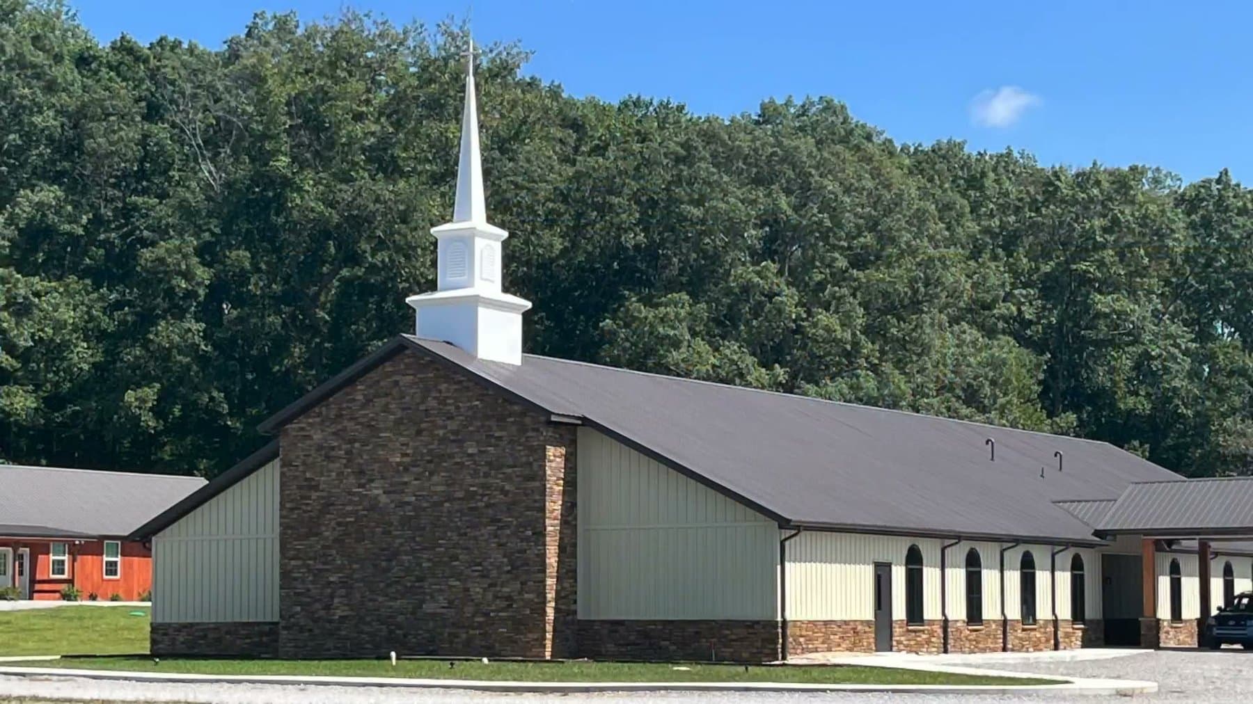 The finished Calvary Baptist Church building — a gabled sanctuary faced in stone, with arched windows and a white steeple, on the drive at 610 Myers Lane