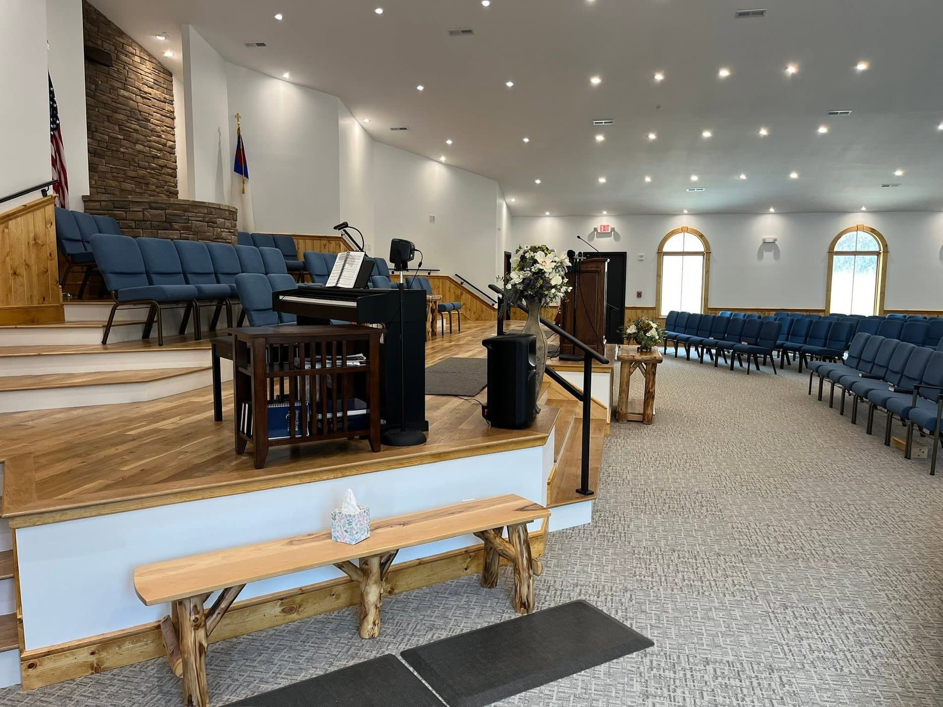 The platform in the auditorium — the piano and organ, choir seating, a stone-faced wall, and log benches at the front